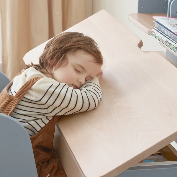 Child resting their head on a wooden height-adjustable desk during a break from schoolwork Child resting their head on a wooden height-adjustable desk during a break from schoolwork