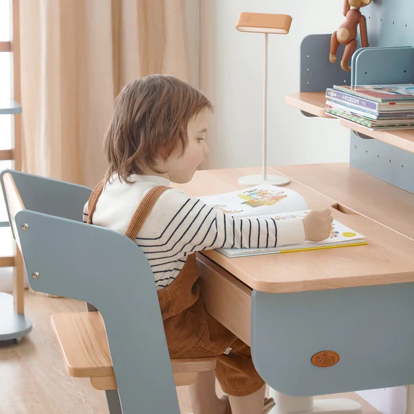 Child sitting in a matching wooden desk and chair set, reading a book at a pegboard-equipped desk Child sitting in a matching wooden desk and chair set, reading a book at a pegboard-equipped desk