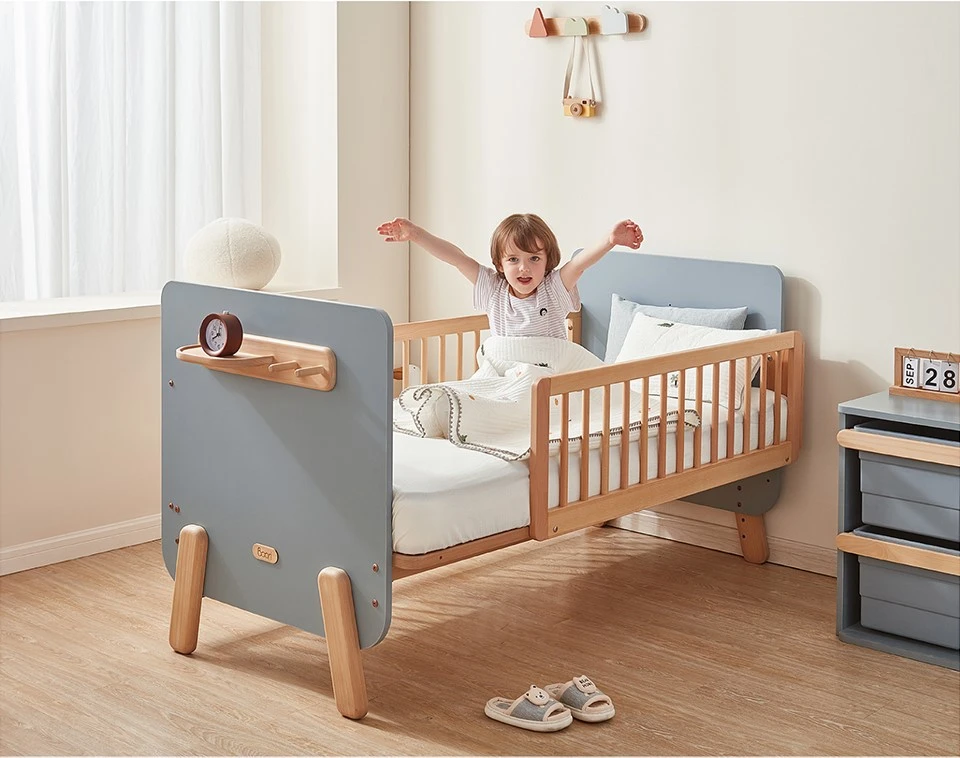 Toddler standing up in a fully railed wooden convertible bed with a headboard shelf and bedside drawer unit nearby Toddler standing up in a fully railed wooden convertible bed with a headboard shelf and bedside drawer unit nearby