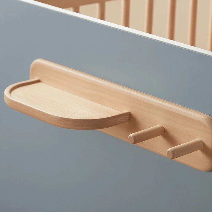 Built-in wooden shelf with hooks attached to the headboard of a convertible kids' bed, holding a small clock Built-in wooden shelf with hooks attached to the headboard of a convertible kids' bed, holding a small clock