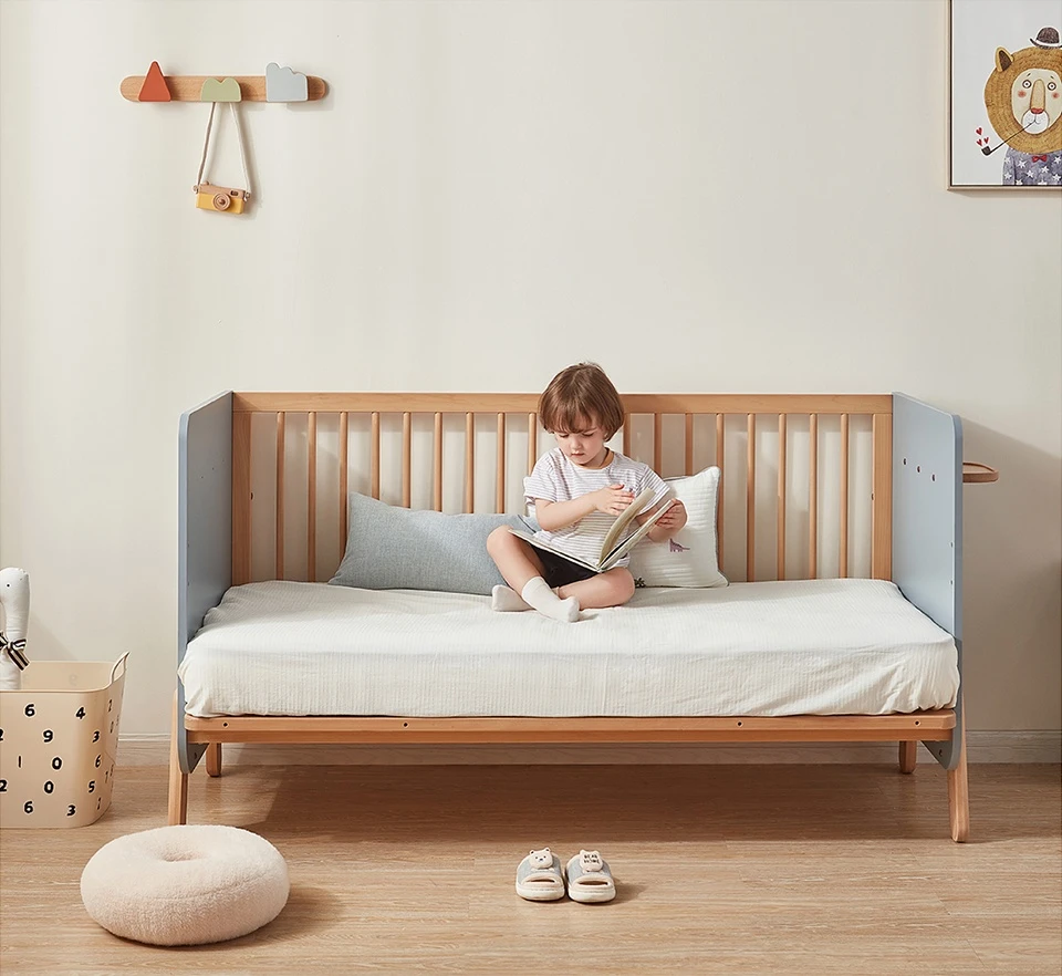 Child sitting and reading on a low wooden daybed, the final stage of a convertible kids' bed with the guardrails removed Child sitting and reading on a low wooden daybed, the final stage of a convertible kids' bed with the guardrails removed