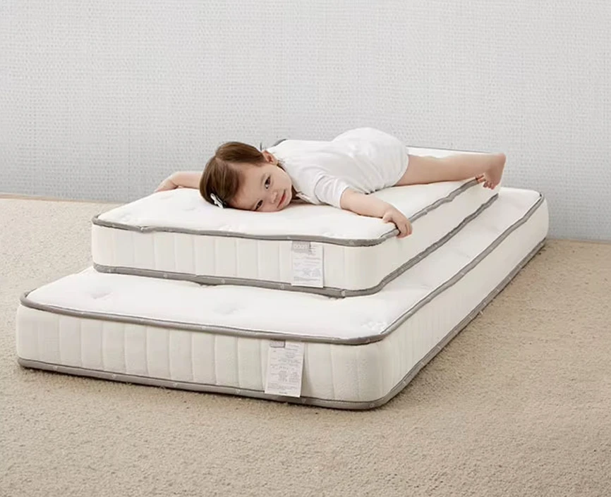 Young child lying on two stacked mattresses on a rug, illustrating the cot bed mattress size required for the cot Young child lying on two stacked mattresses on a rug, illustrating the cot bed mattress size required for the cot