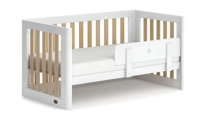 White wooden cot bed in toddler form with a guard panel fitted along the open side White wooden cot bed in toddler form with a guard panel fitted along the open side