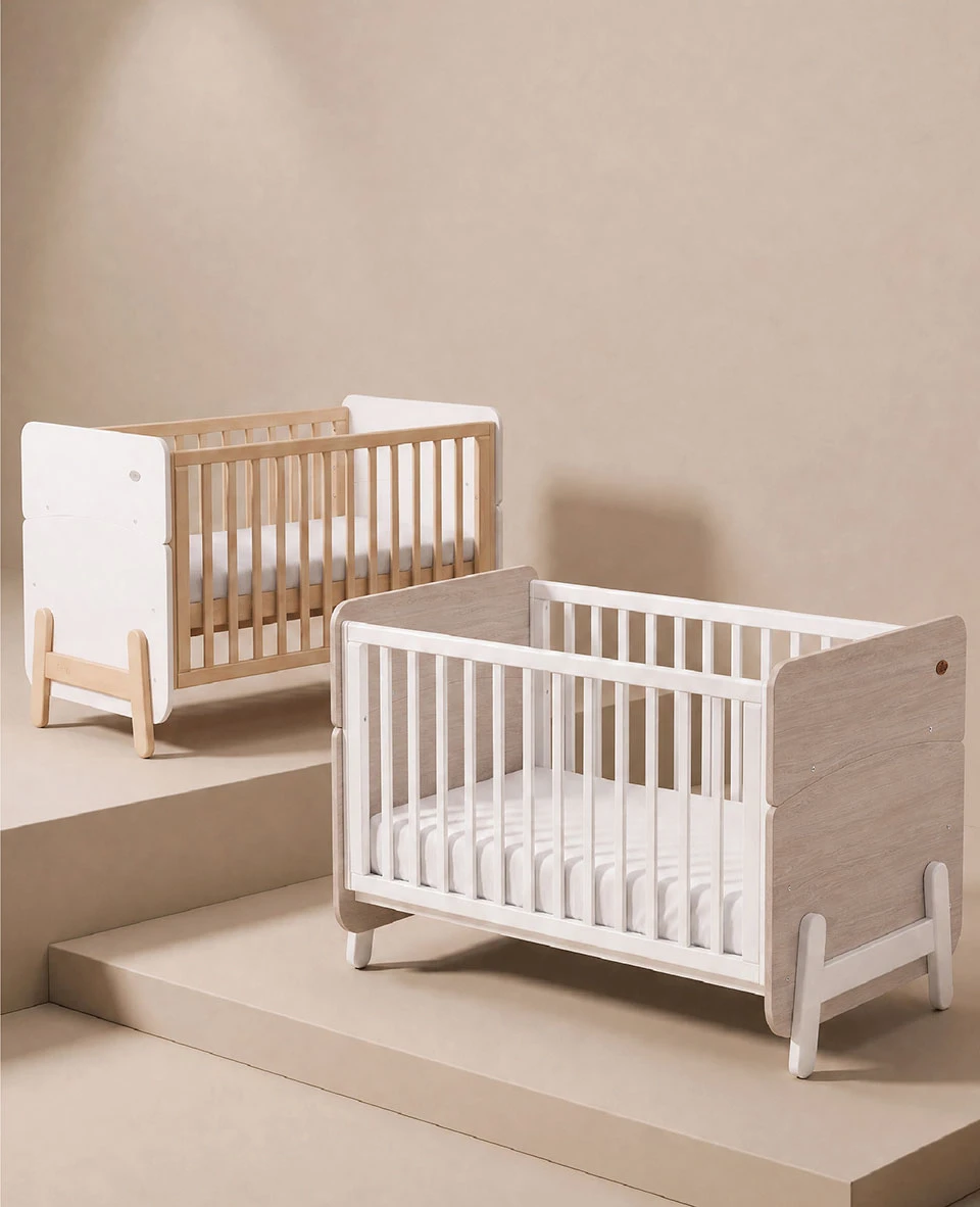 Two wooden baby cots side by side, one with natural timber slats and white end panels and one with white slats and wood-grain end panels Two wooden baby cots side by side, one with natural timber slats and white end panels and one with white slats and wood-grain end panels